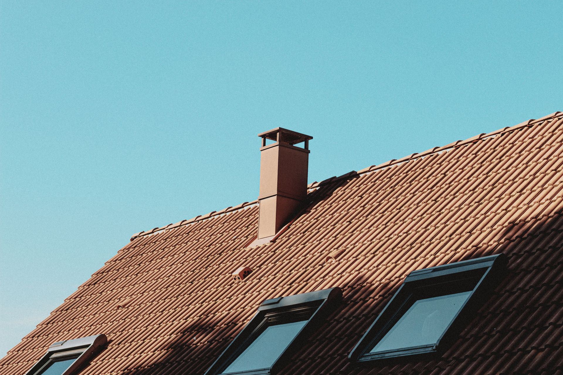 House roof with a chimney and attic windows against a blue sky