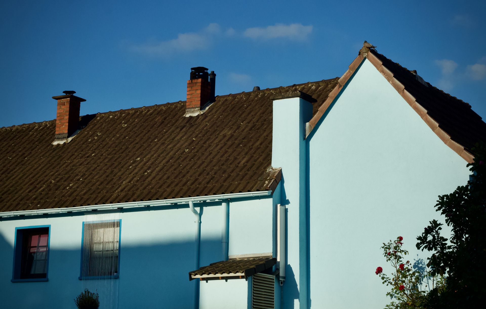 Blue house with a brown roof and chimney under a blue sky